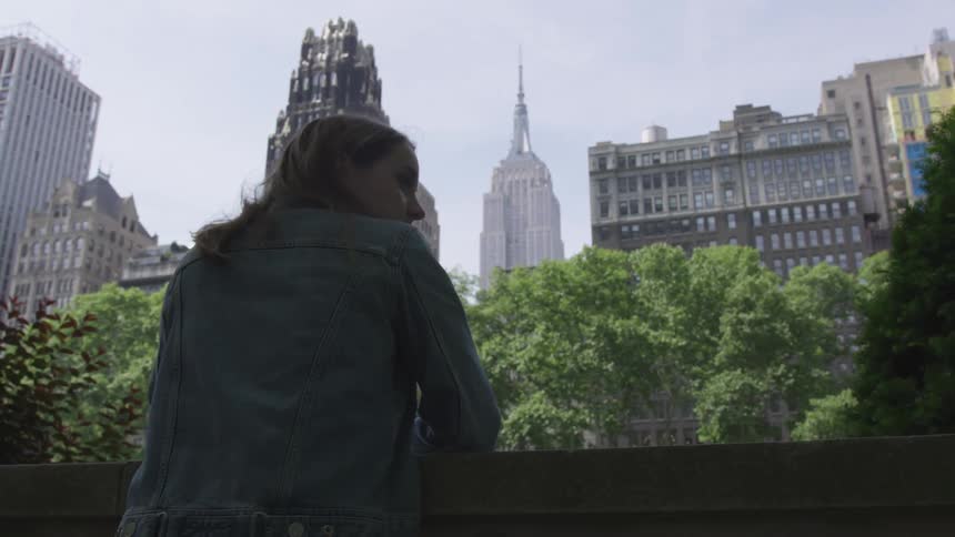 A woman looks over her shoulder as she stands before several tall buildings