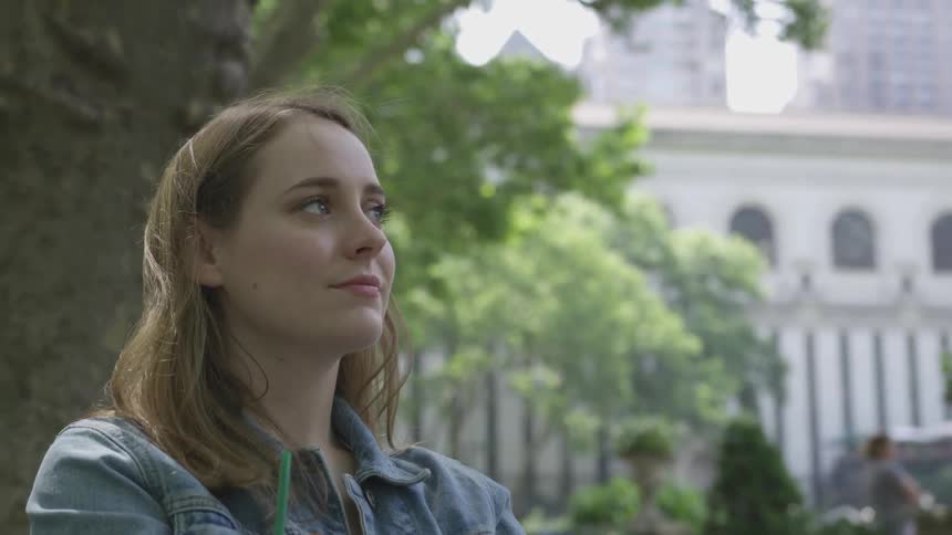 Young woman sitting in city park with buildings in background