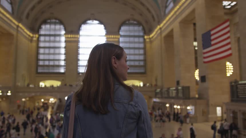 A young white woman looks around a train station