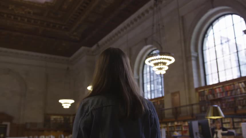 A young woman stands and looks around a library