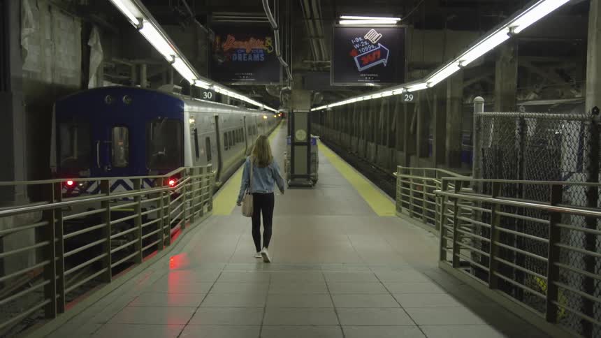 A young white woman with a purse walks into an empty subway station by herself