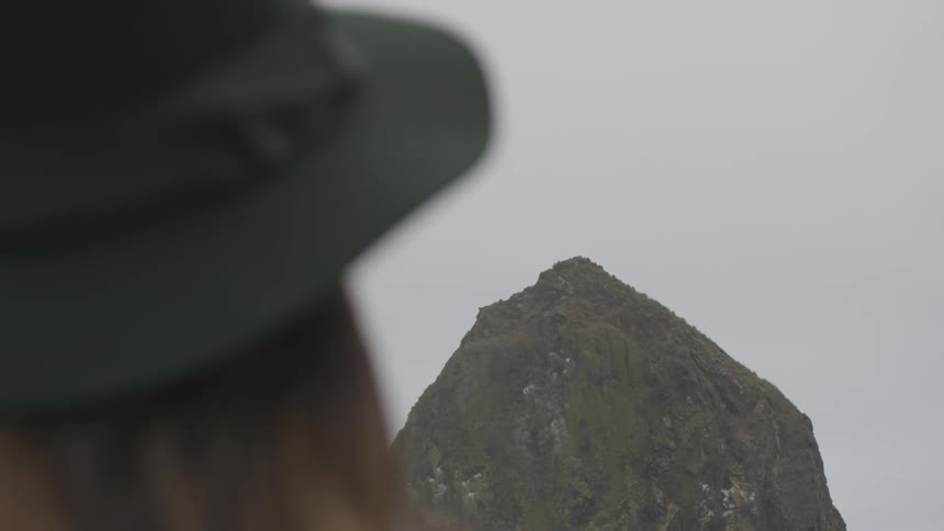 A woman in a green hat staring at a cliff