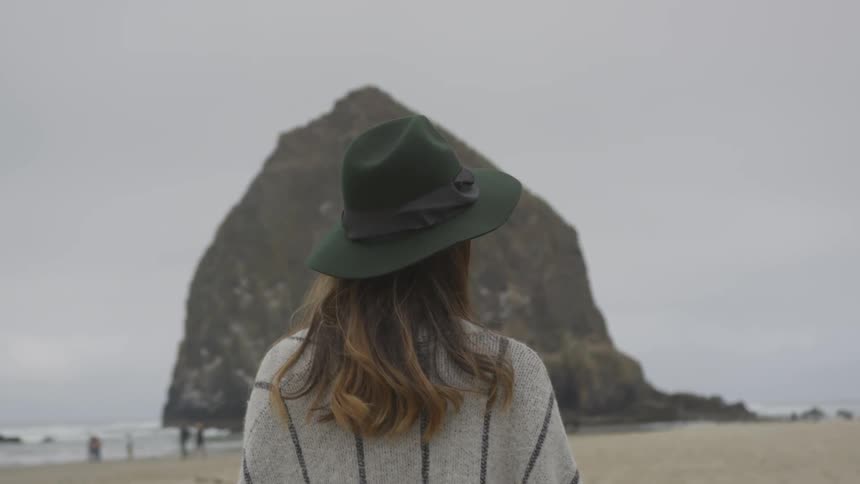 A woman stands on a beach looking around