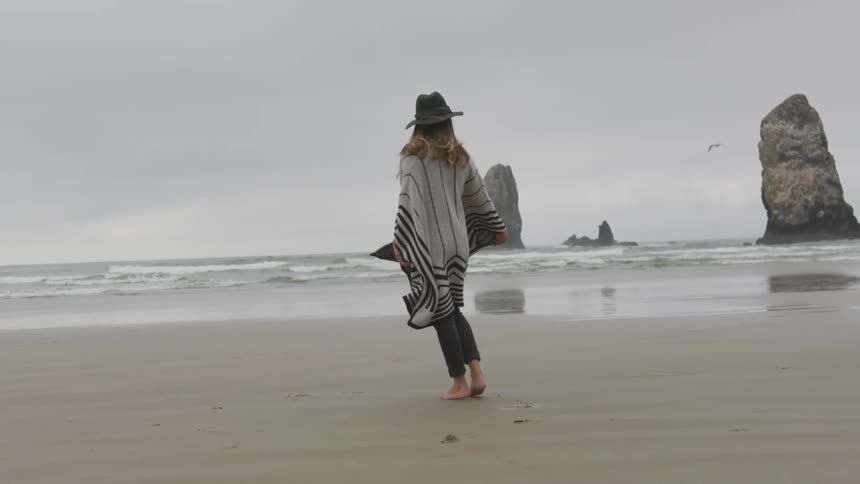 Girl wearing a poncho and hat dancing on the shore at the beach