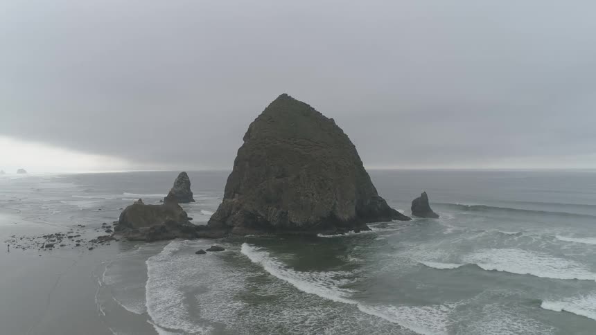 Ocean waves break against rocks and splash as they come to shore on a cloudy gray day