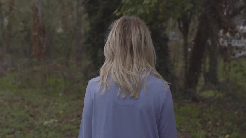 Blonde woman walking in the grass towards a tree in a public park