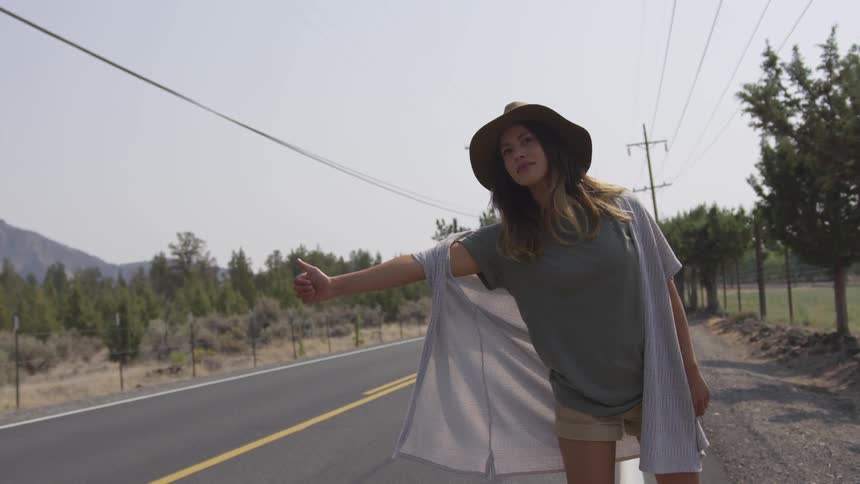 Woman wearing wide hat hitchhikers on the road during the daytime