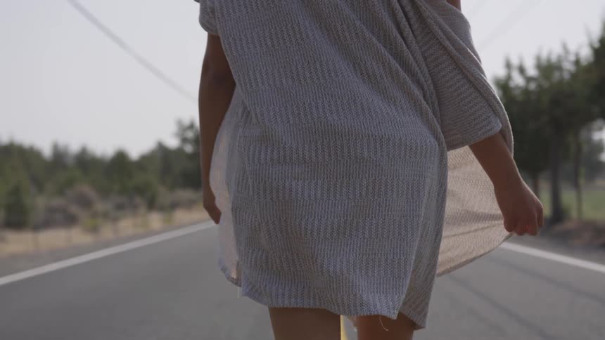 A white woman wearing a flowing robe walks down a street