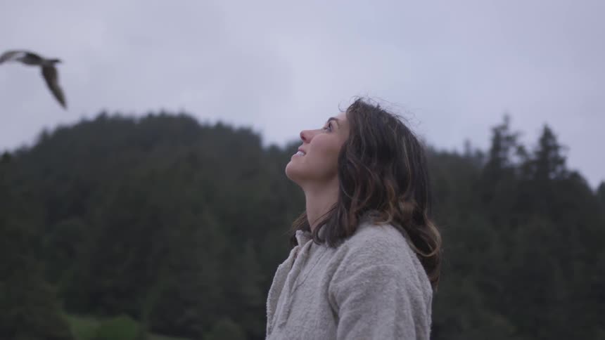 Woman outdoors looking at the sky while a seagull passes by
