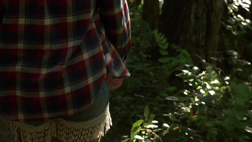 Woman wearing striped shirt walks on forest path by day