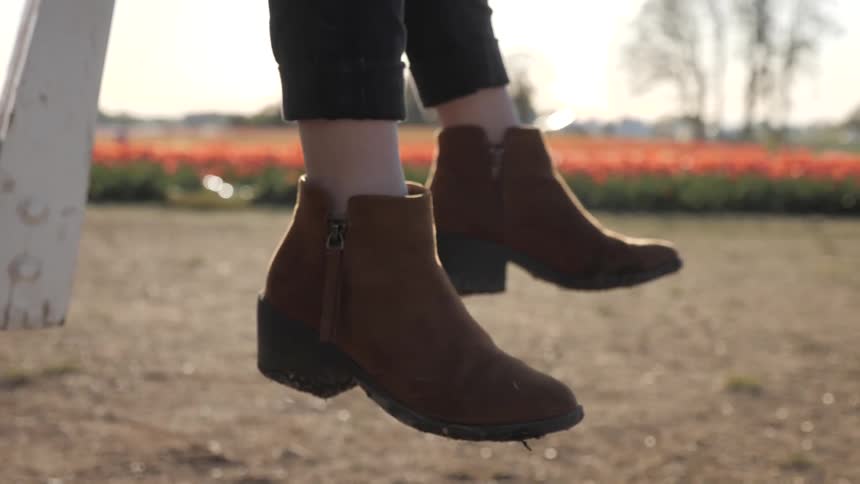 A person wearing brown ankle boots swings their legs