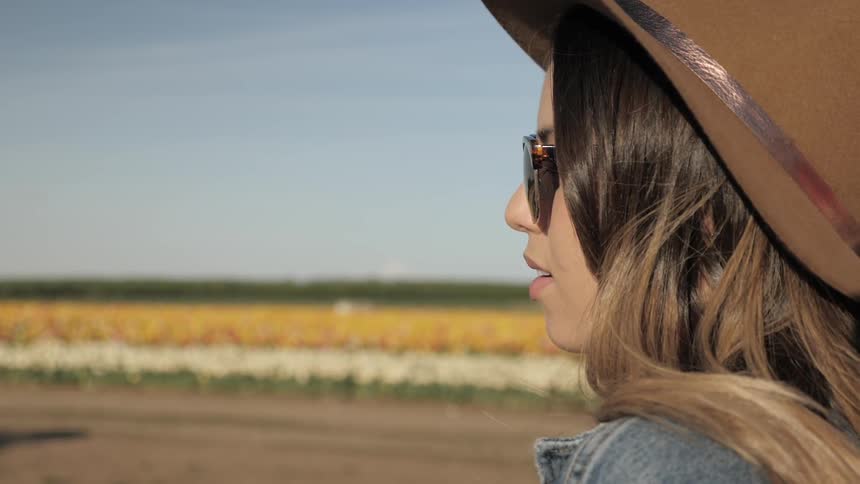 Woman wearing hat stares toward field of flowers