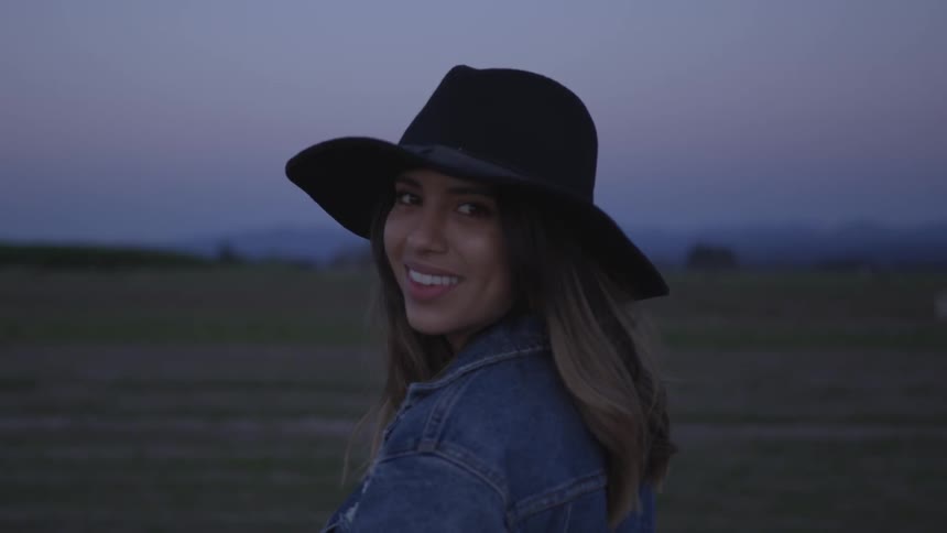 A woman wearing a cowboy hat turns and smiles