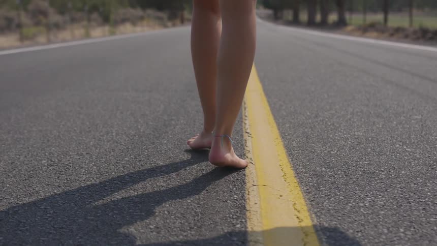 A woman is walking barefoot down a road