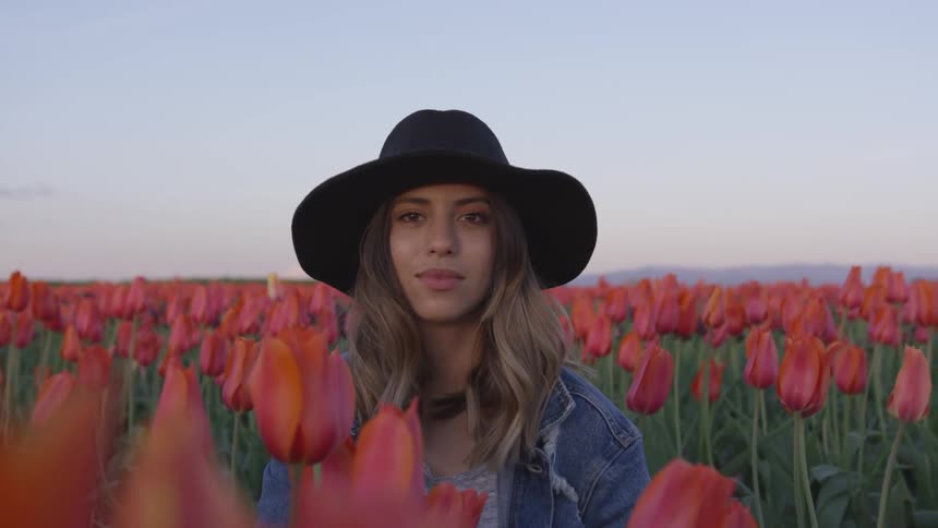 A lady in a black hat looks up from a field of tulips