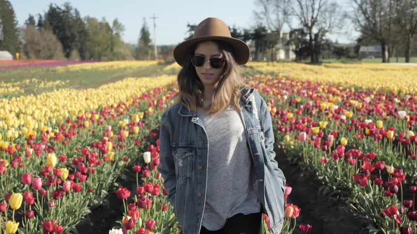 Young woman in a brown hat and denim jacket walking through a field of tulips