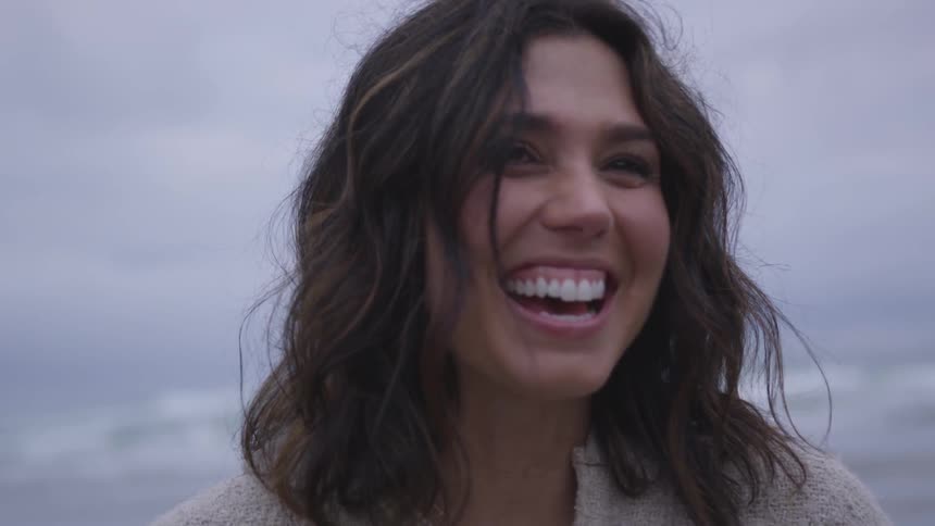 A dark haired female laughing on the beach