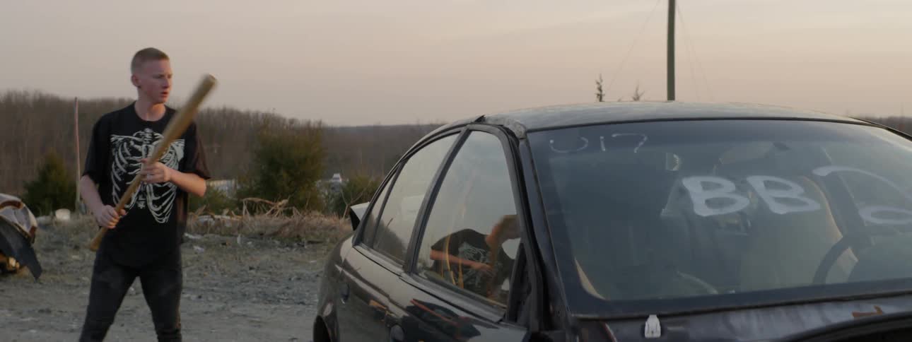 A teenager smashes the windows of a car with a bat