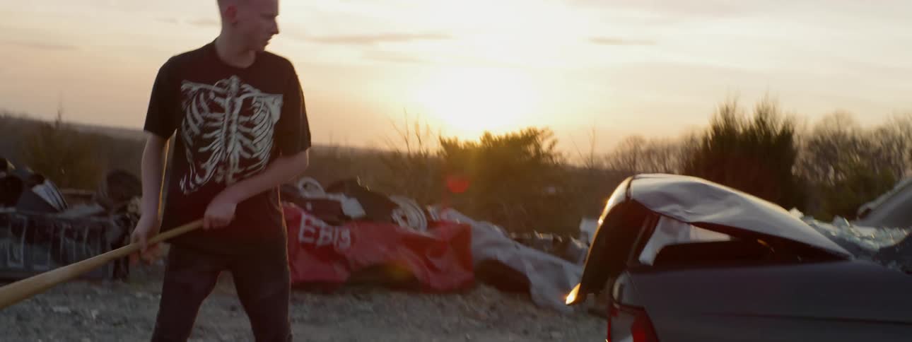 A man is smashing a vehicle with a baseball bat