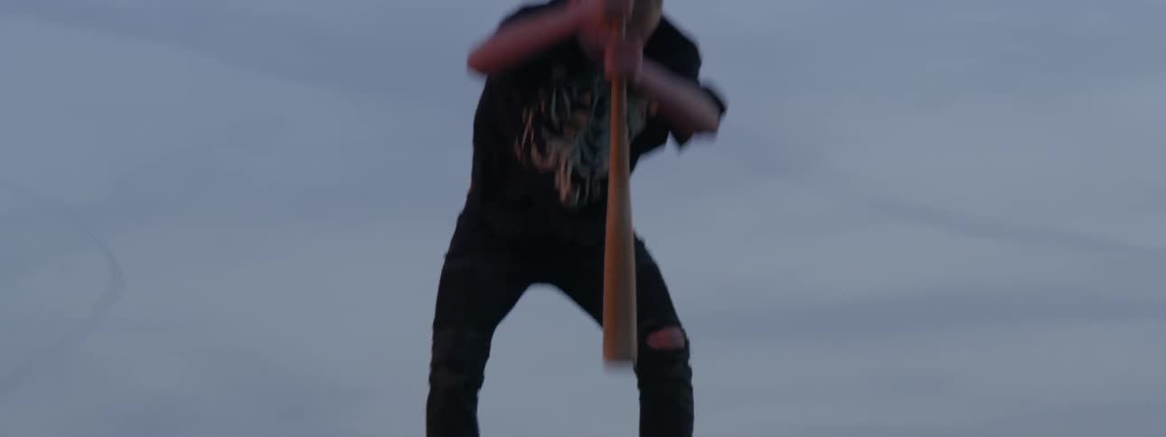 The young man is standing on top of the vehicle with a baseball bat he is repetitively beating the vehicles windshield with a baseball bat