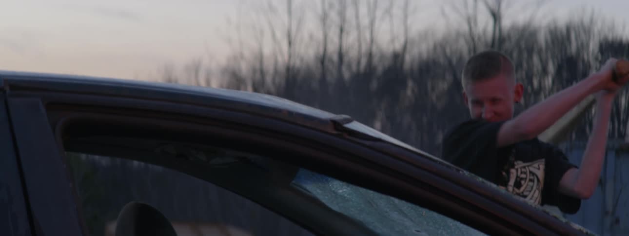 A teenager destroys a car windshield with a baseball bat