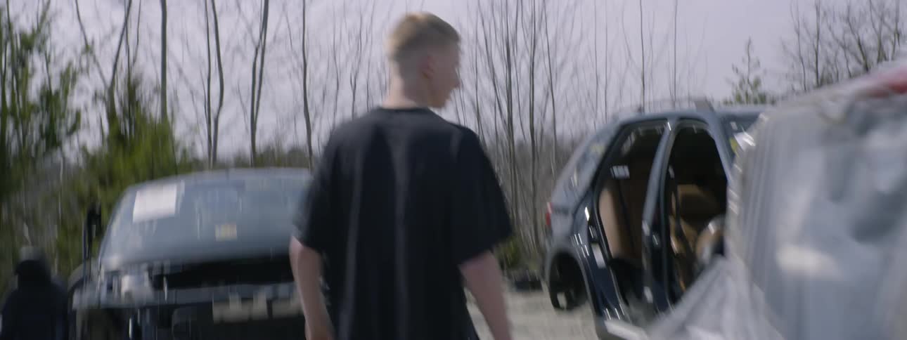 Boy wearing black t shirt walks aggressively in junkyard and puts his hand behind his head during the daytime