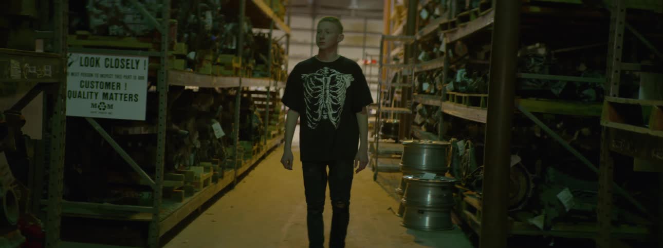 A teenager walks through a large warehouse full of used auto parts on wooden shelving