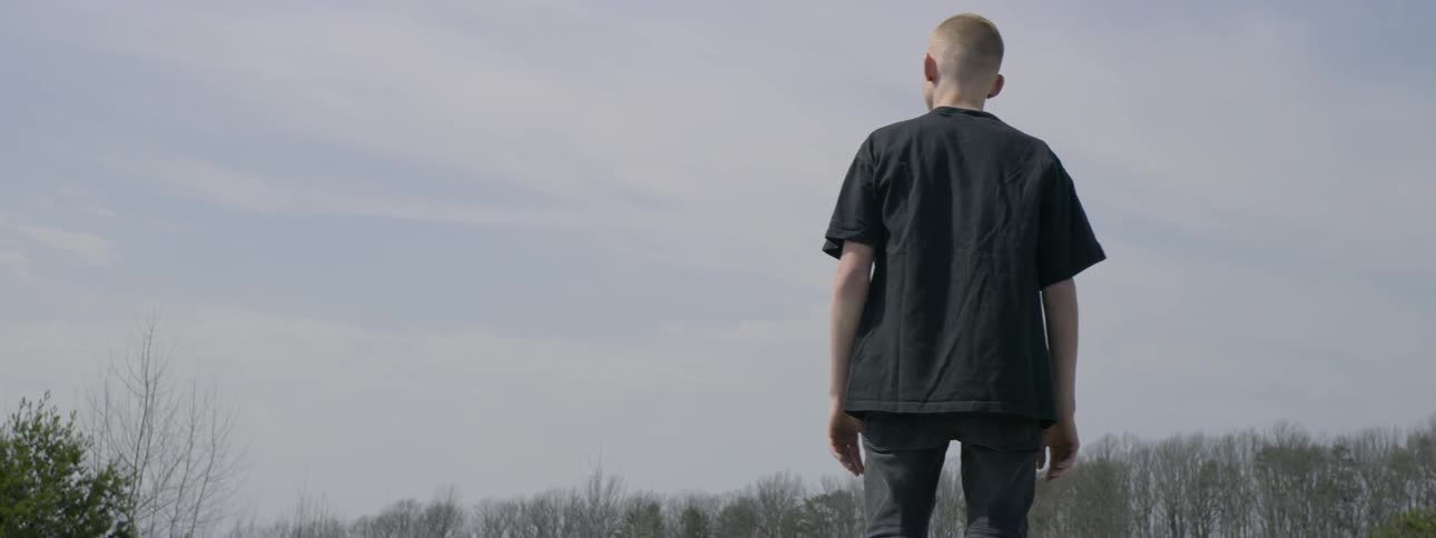 A young man crouches on top of a car in a parking lot