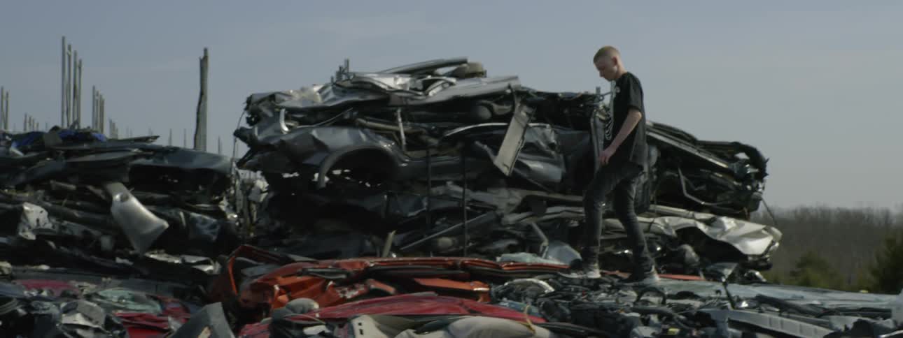 Teenager climbs onto a pile of old cars in a car scrap yard