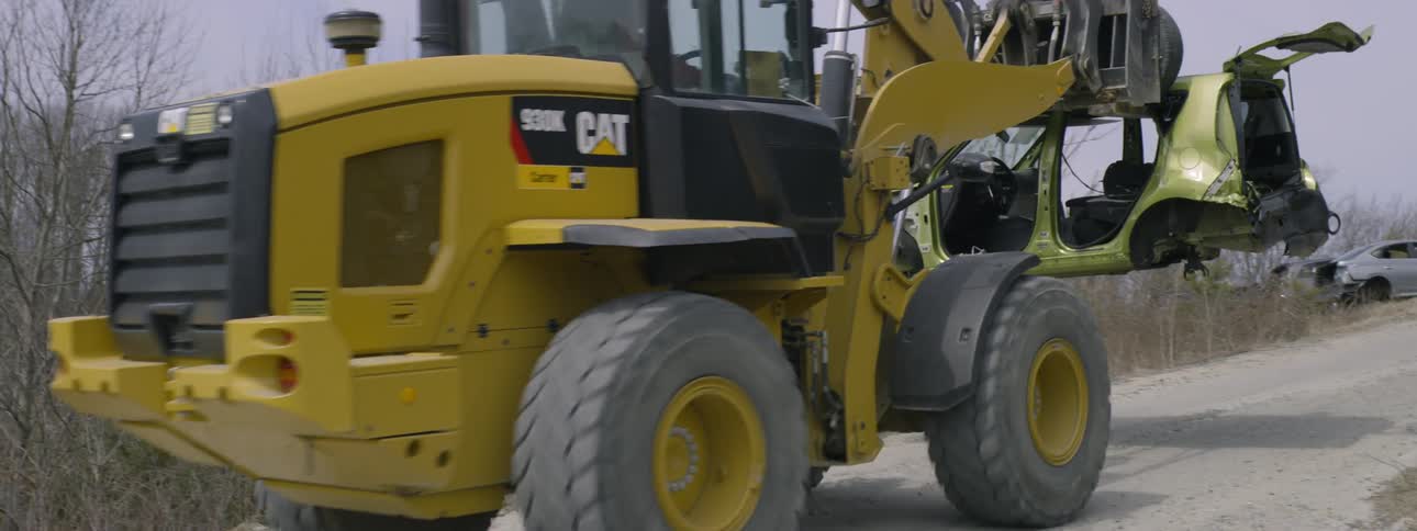 A tractor carries a smashed up car along a road