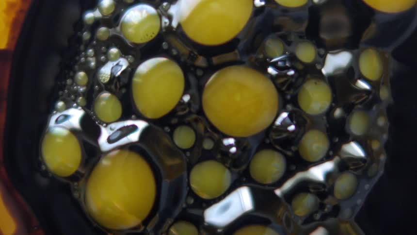 Yellow bubbles burst and rotate in black liquid
