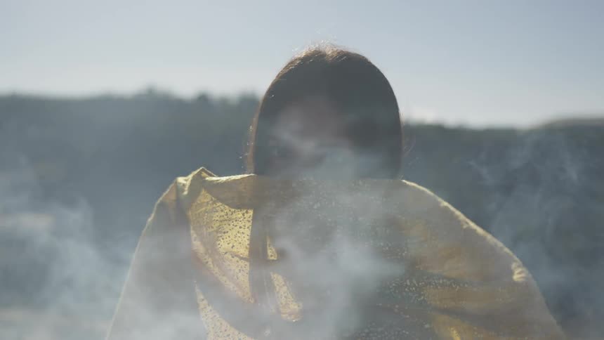 The woman is holding a yellow cloth over her face and looking directly at the camera
