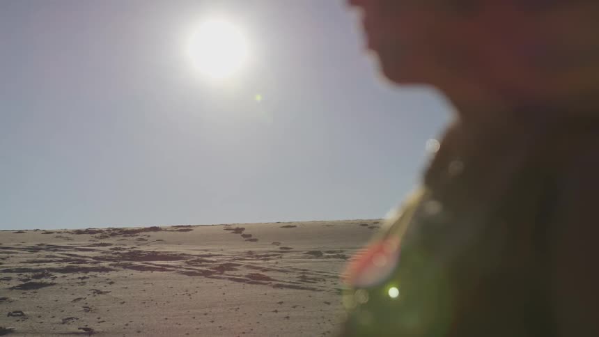 Blonde woman stands on yellow sand while the shining sun goes down