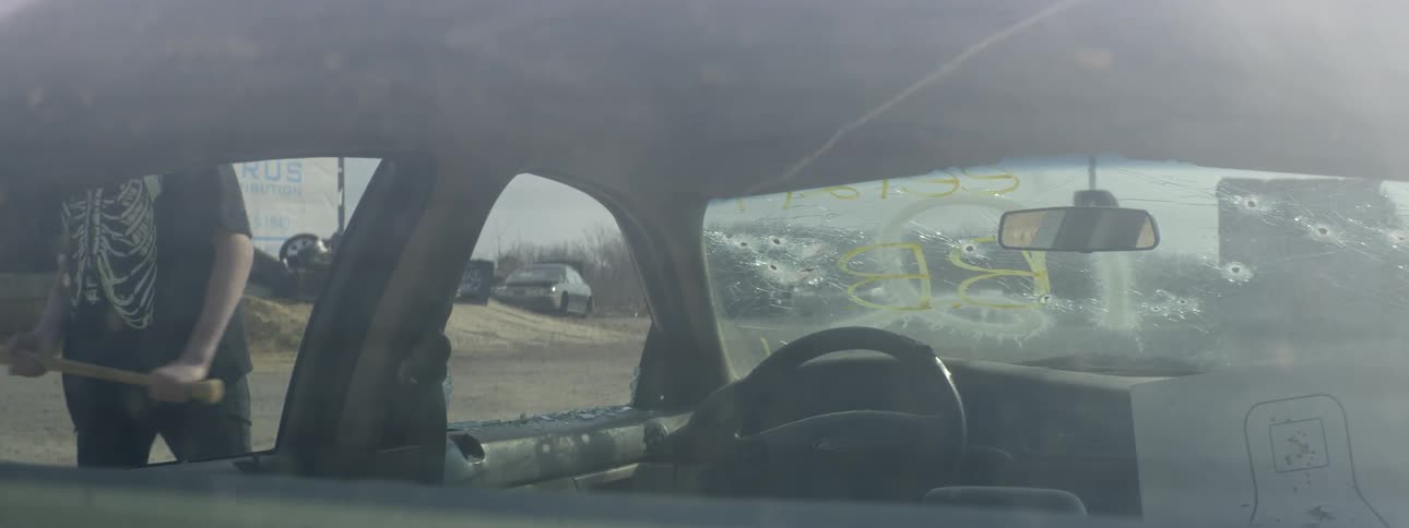A person smashes out a car window with a bat