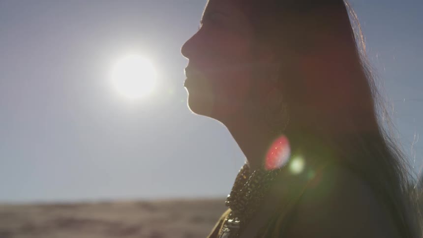 A woman looks up at the sky as the sun sets behind her