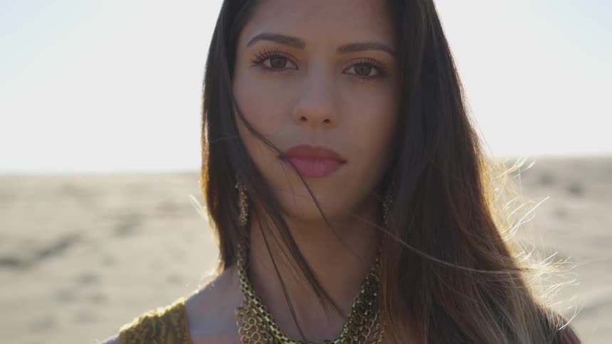 A woman stands in the desert with the sun setting behind her
