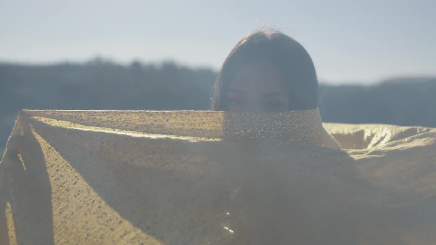 A woman holds a scarf up and twirls it against her face