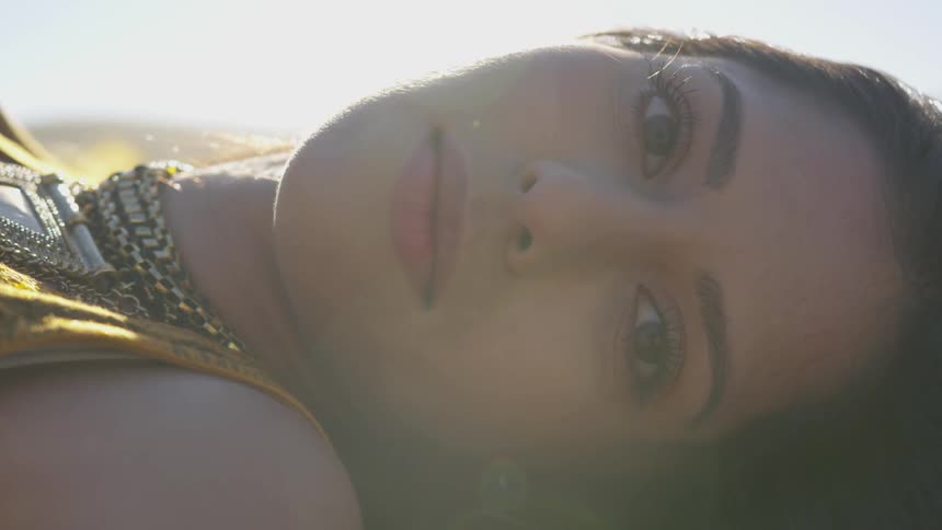 Brunette woman lying down on the ground turns her face while the sun shines on her cheek