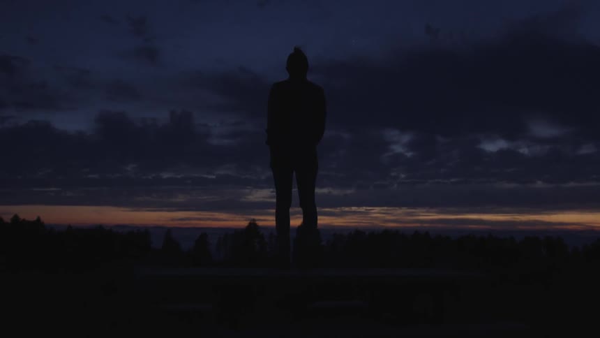 A silhouetted man looks out towards the horizon at dusk