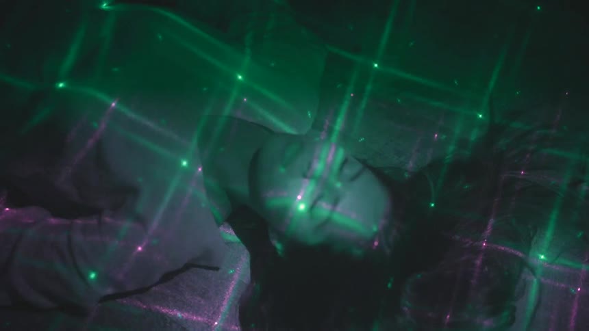 A woman laying down with her eyes closed while a pink and green laser show flashes