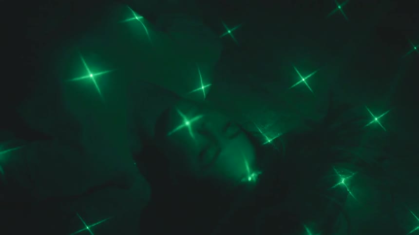 A woman lays on the floor while lights move all around her