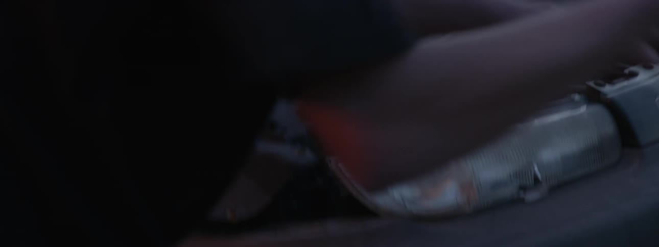 A man smashes out the headlight of a junked car with a baseball bat