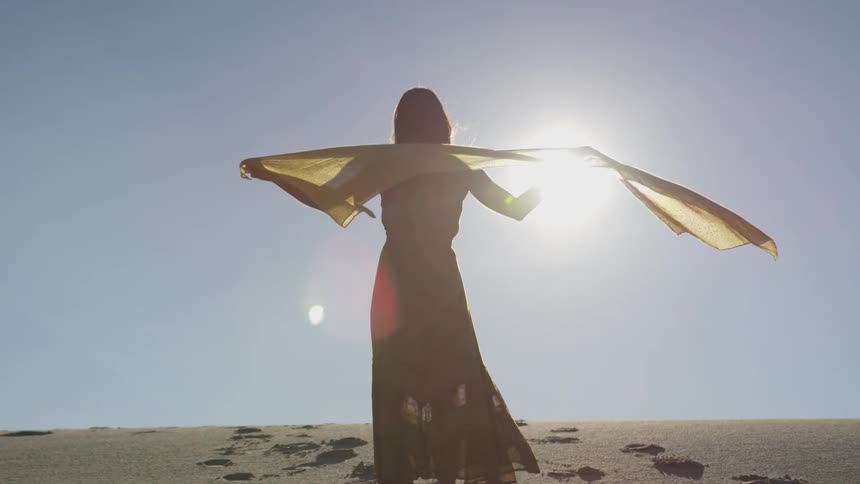 Woman stands in the middle of a desert and her scarf sways in the wind