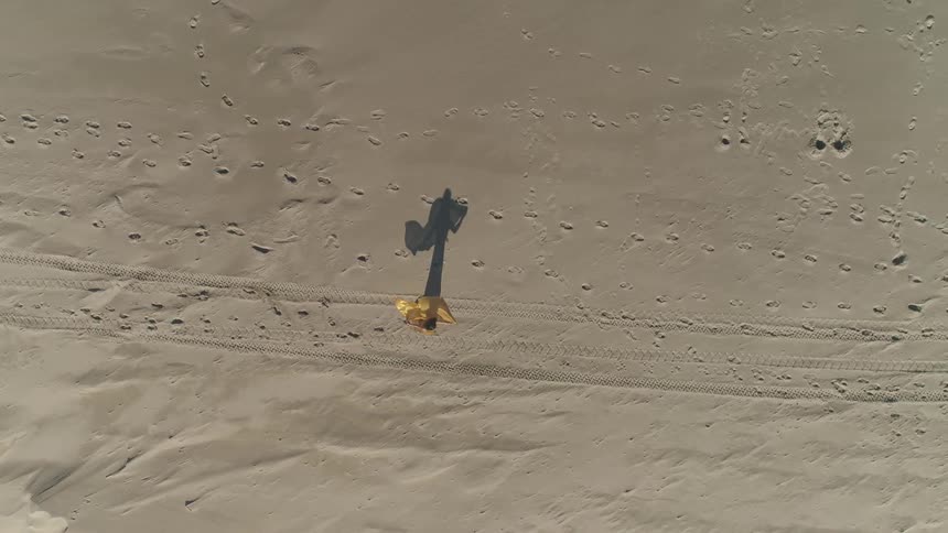 Woman with flowing cloth twirls on sand dotted with tracks and footprints