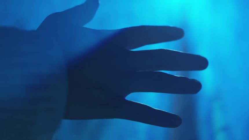 A hand reaches out toward a bright light in a blue lit room