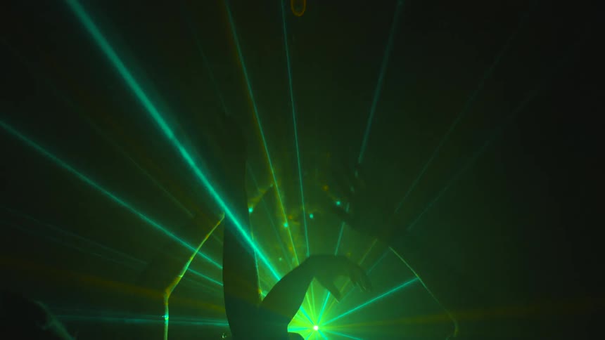 People dancing and waving their arms through lasers