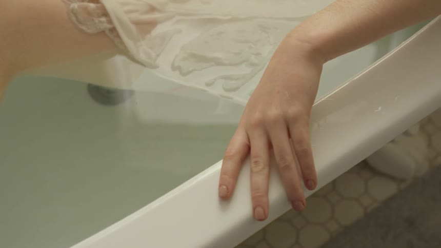 A woman soaking in a bathtub wearing a dress