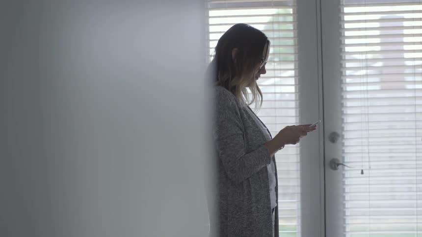 A woman standing inside typing on her smartphone