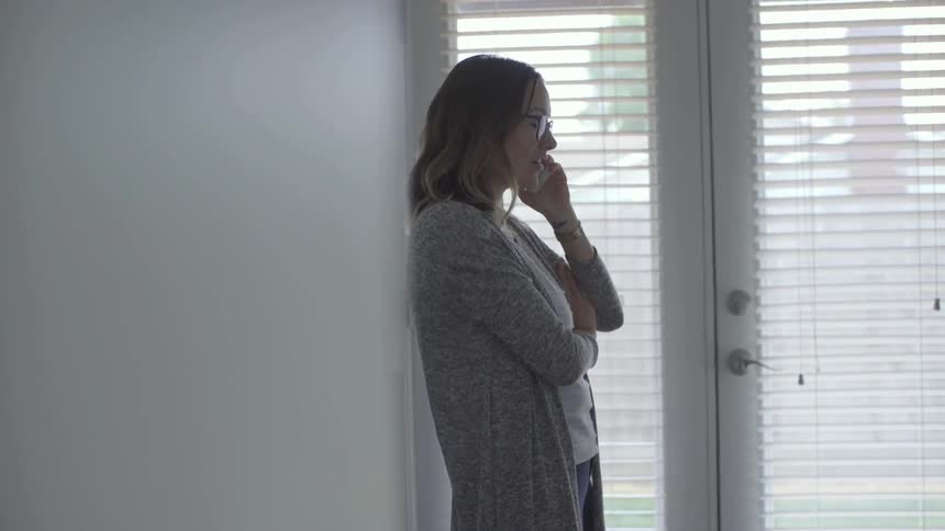 A white woman with glasses stands in a room and talks on a cell phone