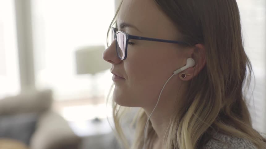 A woman indoors listening to music on her earbuds